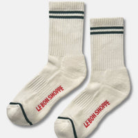 A pair of ribbed crew socks in off-white, featuring two dark green stripes near the cuff, a dark green toe stripe, and the brand name 'LE BON SHOPPE' printed in red on the sole of each sock.