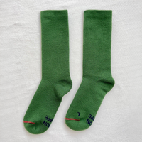 A pair of green crew socks laid flat on a white textured background, with dark navy text and a thin red stripe near the toes.