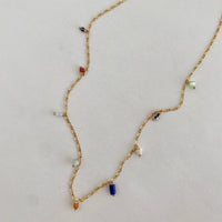 Gold necklace with colorful beads on a light gray background