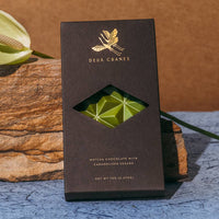 Dark chocolate bar with green candy inside, branded 'Devu Chocolates', on a textured surface with decorative elements.