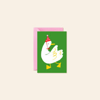 A greeting card with a pink envelope behind it, featuring a white cartoon duck wearing a red and white party hat