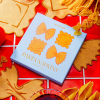 Pasta-shaped napkins on a red checkered tablecloth with pasta pieces around.