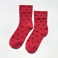 A pair of red crew socks with a repeating pattern of small black hearts, displayed on a clean white background.