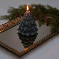 Tree-shaped candle on a reflective surface with a mirror and greenery in the background