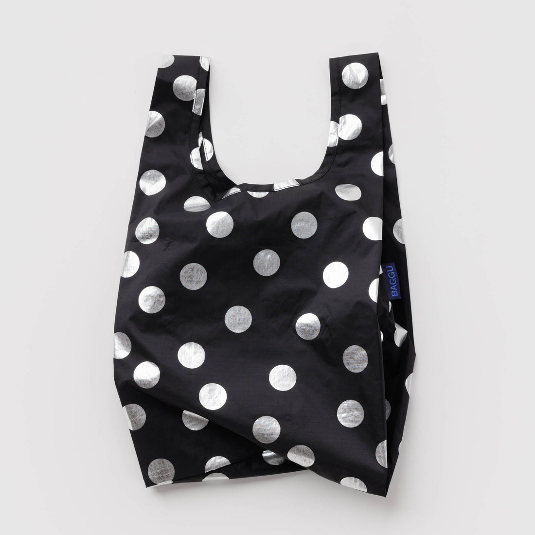 A reusable tote bag with a black base and large silver polka dots, photographed flat against a light gray background.