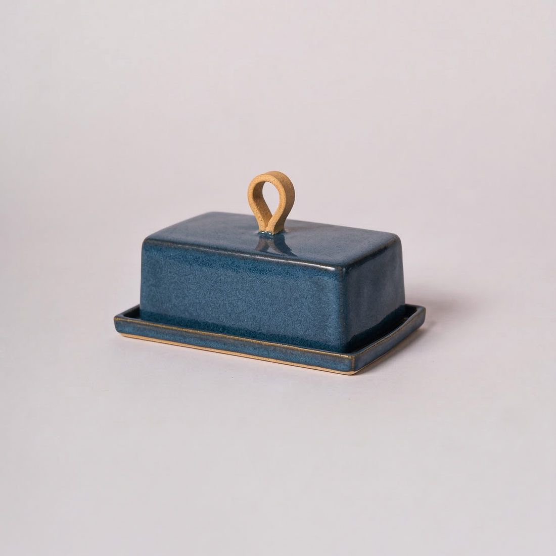 Blue ceramic butter dish with a wooden handle on a light gray background