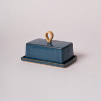 Blue ceramic butter dish with a wooden handle on a light gray background