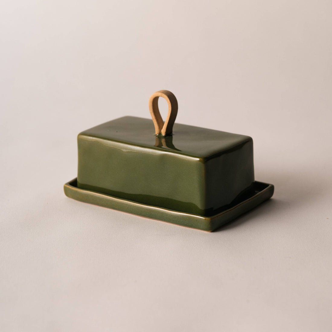 A rectangular green ceramic butter dish with a matching base and a small loop handle on top, photographed on a plain light beige background.