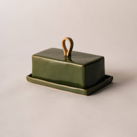 A rectangular green ceramic butter dish with a matching base and a small loop handle on top, photographed on a plain light beige background.