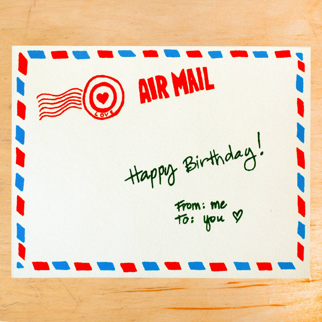Handwritten 'Happy Birthday!' card on a paper with air mail envelope design