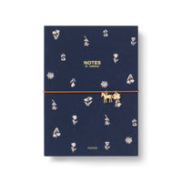 A navy blue hardcover A5 notebook with a gold elastic closure strap and a small gold horse charm. The cover features a delicate pattern of white flowers