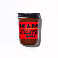A jar of Fine & Raw dark chocolate hazelnut butter spread with a red label and black lid, photographed on a white background with a soft shadow.