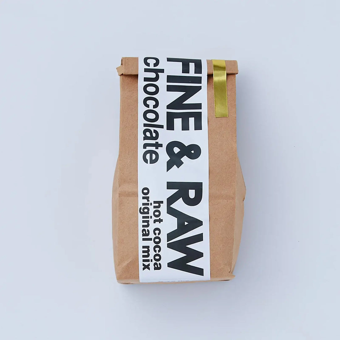 A brown kraft paper bag of Fine & Raw Hot Cocoa Original Mix, featuring a white label with bold black text and a gold ribbon accent, set against a clean light gray background.