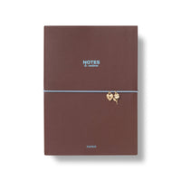 A brown PU soft cover notebook with a light blue elastic band and small gold leaf charms