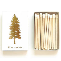 White match box with a gold foiled spruce tree and blue spruce lettering below it