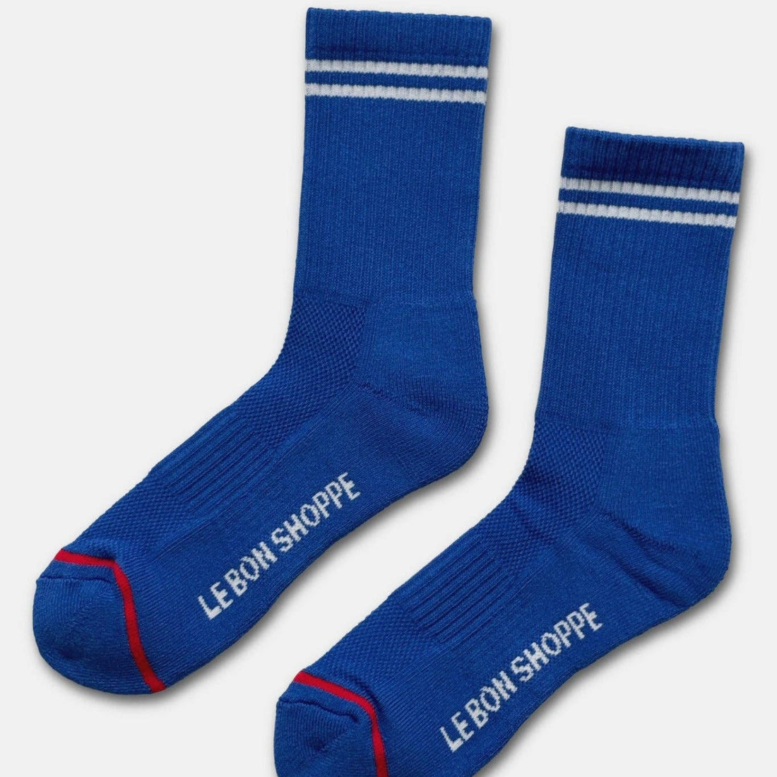 A pair of royal blue crew socks with white stripes near the cuff, white 'LE BON SHOPPE' branding on the toes, and red toe accents, displayed on a light gray background.