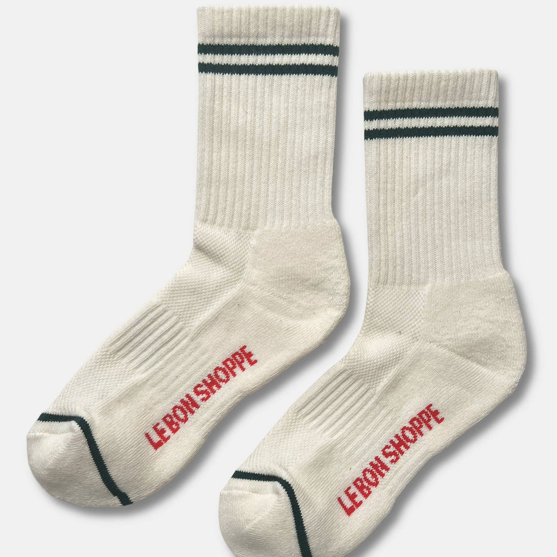 A pair of ribbed crew socks in off-white, featuring two dark green stripes near the cuff, a dark green toe stripe, and the brand name 'LE BON SHOPPE' printed in red on the sole of each sock.