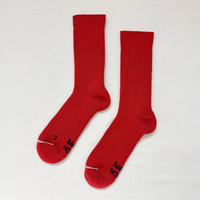 A pair of bright red crew socks laid flat on a white textured background, with black text printed on the toes and heels.