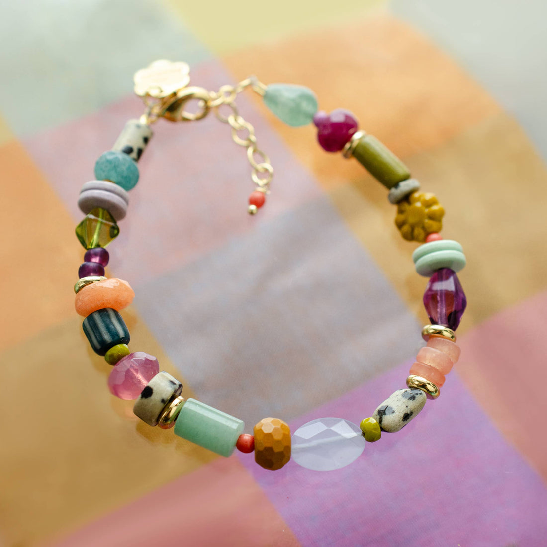 A colorful beaded bracelet with a gold clasp, featuring various stone beads in green, pink, purple, orange, and white.