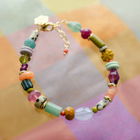 A colorful beaded bracelet with a gold clasp, featuring various stone beads in green, pink, purple, orange, and white.