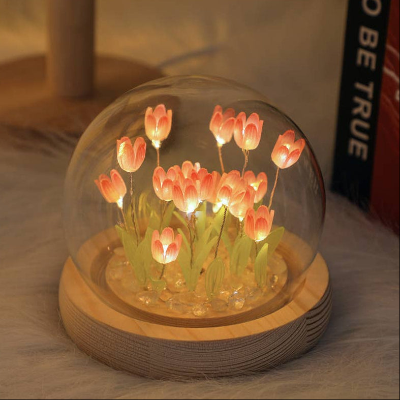 Decorative glass dome with glowing pink tulips on a wooden base.