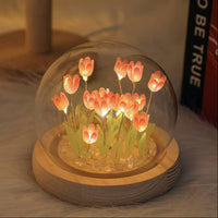Decorative glass dome with glowing pink tulips on a wooden base.