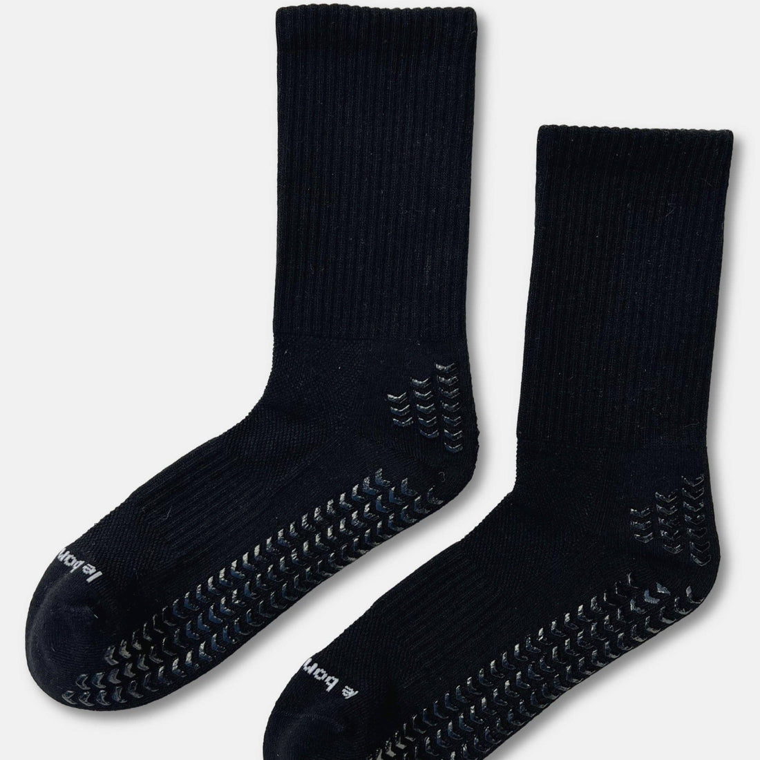 A pair of black grip socks with textured non-slip patterns on the sole and toe, displayed against a light gray background.
