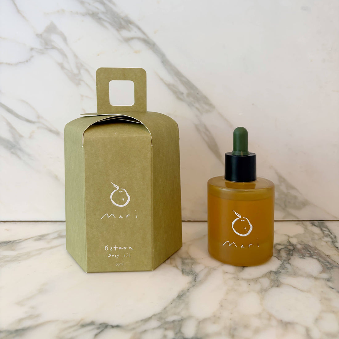 Bottle of MARI oil with its packaging on a marble surface