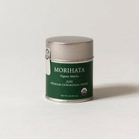 A small cylindrical metal tin of Morihata Organic Matthu Jun Premium Ceremonial Grade tea, featuring a dark green label and a brushed silver lid, set against a plain light gray background.