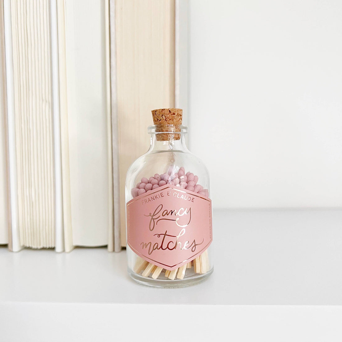 Glass bottle with cork lid containing pink matches and a decorative label 